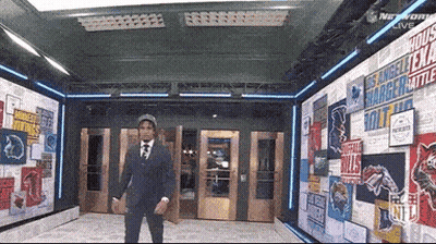 A Man In A Suit And Tie Is Standing In Front Of A Wall With Nfl Logos GIF