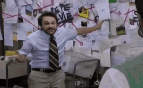 A Man In A Suit And Tie Is Standing In Front Of A Wall With Papers On It . GIF