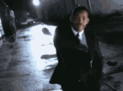 A Man In A Suit And Tie Is Standing In Front Of A White Car GIF