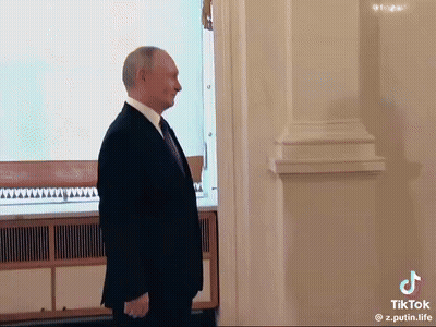 A Man In A Suit And Tie Is Standing In Front Of A White Wall . GIF