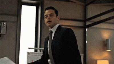 A Man In A Suit And Tie Is Standing In Front Of A Window . GIF