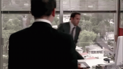 A Man In A Suit And Tie Is Standing In Front Of A Window Looking Out GIF