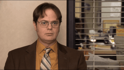 A Man In A Suit And Tie Is Standing In Front Of A Window With Blinds GIF
