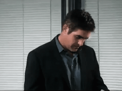 A Man In A Suit And Tie Is Standing In Front Of A Window With Blinds . GIF