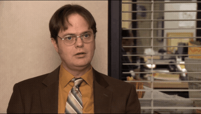 A Man In A Suit And Tie Is Standing In Front Of A Window With Blinds GIF