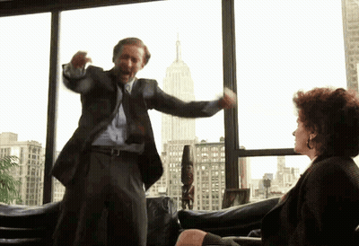 A Man In A Suit And Tie Is Standing In Front Of A Woman In A Chair GIF
