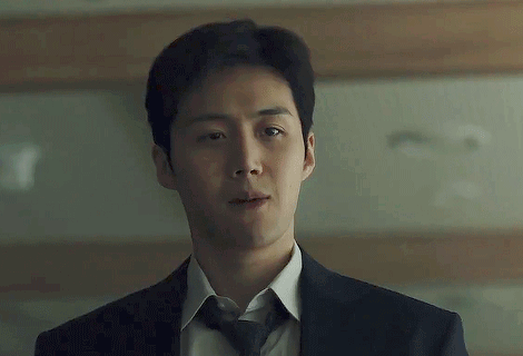 A Man In A Suit And Tie Is Standing In Front Of A Wooden Wall . GIF