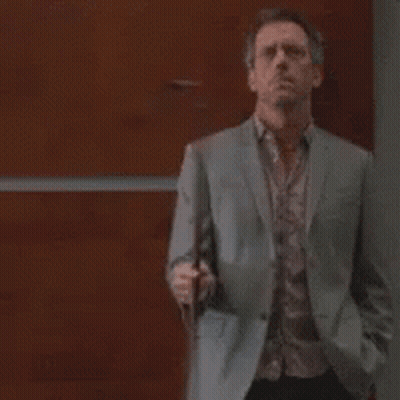 A Man In A Suit And Tie Is Standing In Front Of A Wooden Wall Holding A Cell Phone . GIF