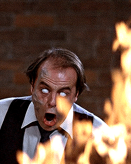 A Man In A Suit And Tie Is Standing In Front Of Flames GIF