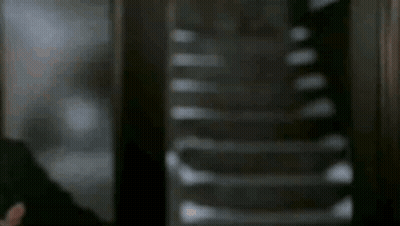 A Man In A Suit And Tie Is Standing In Front Of Stairs . GIF