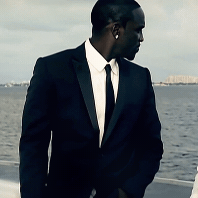 A Man In A Suit And Tie Is Standing In Front Of The Water GIF