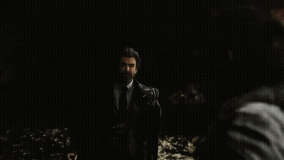 A Man In A Suit And Tie Is Standing In The Dark And Looking At Another Man . GIF
