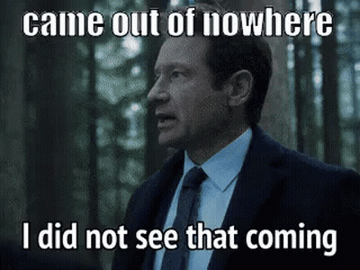 A Man In A Suit And Tie Is Standing In The Woods Looking At Something . GIF