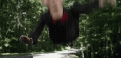 A Man In A Suit And Tie Is Standing In The Woods With His Hands Outstretched . GIF