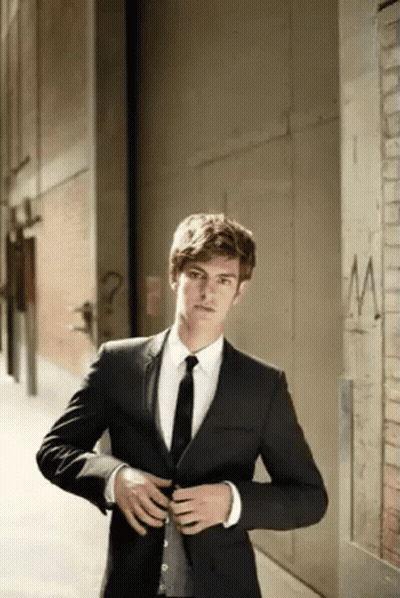 A Man In A Suit And Tie Is Standing Next To A Brick Wall . GIF