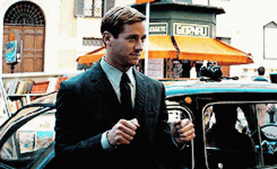 A Man In A Suit And Tie Is Standing Next To A Car In Front Of A Store That Says Gornelli GIF
