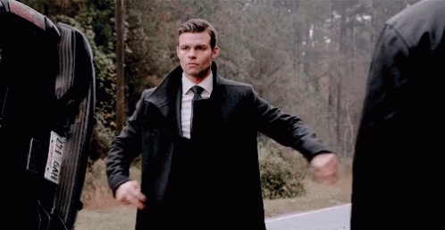 A Man In A Suit And Tie Is Standing Next To A Man In A Black Coat . GIF