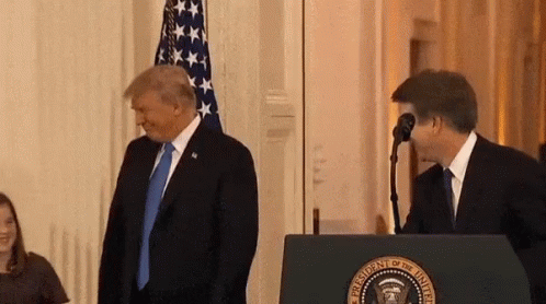 A Man In A Suit And Tie Is Standing Next To A Man In A Suit Behind A Podium . GIF