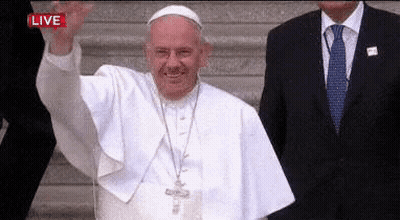 A Man In A Suit And Tie Is Standing Next To A Man In A White Robe Waving . GIF
