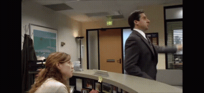 A Man In A Suit And Tie Is Standing Next To A Woman At A Reception Desk In Front Of An Exit Sign GIF