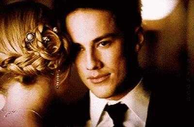 A Man In A Suit And Tie Is Standing Next To A Woman In A Braided Bun GIF