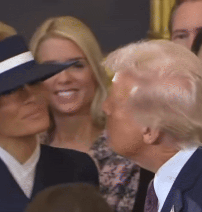 A Man In A Suit And Tie Is Standing Next To A Woman In A Hat GIF