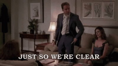 A Man In A Suit And Tie Is Standing Next To A Woman On A Couch In A Living Room . GIF