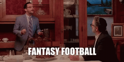 A Man In A Suit And Tie Is Standing Next To Another Man At A Table And Says Fantasy Football . GIF