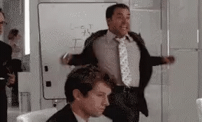 A Man In A Suit And Tie Is Standing Next To Another Man In A Chair In Front Of A Whiteboard . GIF