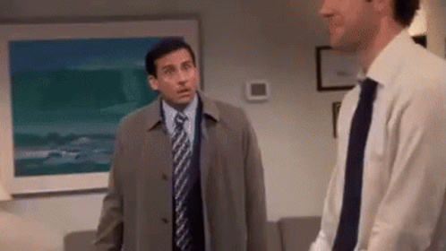 A Man In A Suit And Tie Is Standing Next To Another Man In A Living Room . GIF