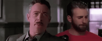 A Man In A Suit And Tie Is Standing Next To Another Man In A Red Shirt In A Room . GIF