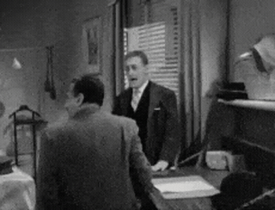 A Man In A Suit And Tie Is Standing Next To Another Man In A Room . GIF