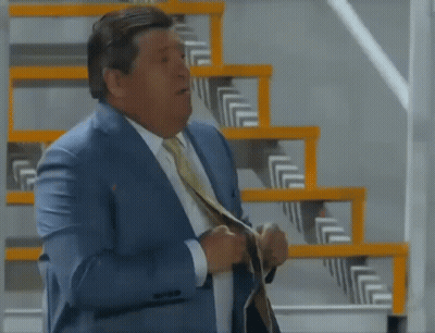 A Man In A Suit And Tie Is Standing Next To Stairs GIF