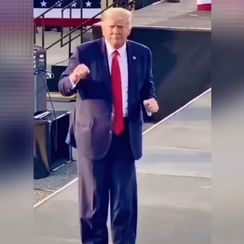 A Man In A Suit And Tie Is Standing On A Stage Giving A Fist Bump GIF