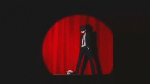A Man In A Suit And Tie Is Standing On A Stage In Front Of A Red Curtain GIF