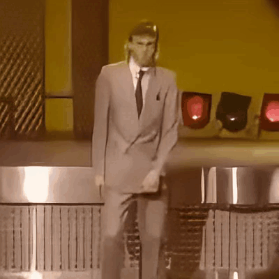 A Man In A Suit And Tie Is Standing On A Stage GIF
