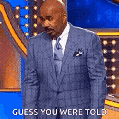A Man In A Suit And Tie Is Standing On A Stage With The Words `` Guess You Were Told '' . GIF