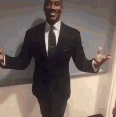 A Man In A Suit And Tie Is Standing With His Arms Outstretched And Smiling GIF