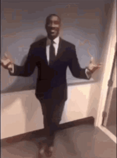 A Man In A Suit And Tie Is Standing With His Arms Outstretched In A Hallway . GIF