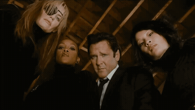 A Man In A Suit And Tie Is Surrounded By Three Women In Black GIF
