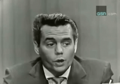 A Man In A Suit And Tie Is Talking In Front Of A Sign That Says Gsn.com GIF