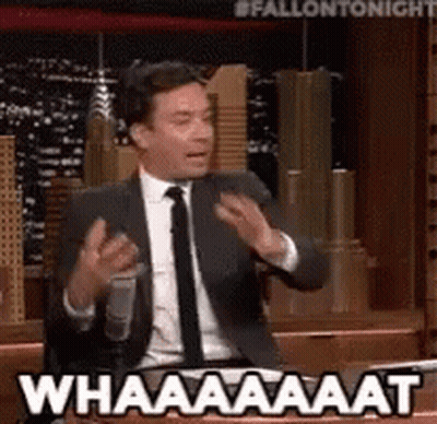 A Man In A Suit And Tie Is Talking Into A Microphone And Saying Whaaaaat GIF