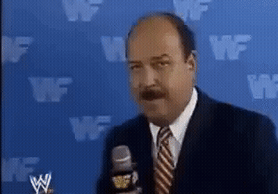 A Man In A Suit And Tie Is Talking Into A Microphone In Front Of A Blue Wall With Wf Written On It . GIF