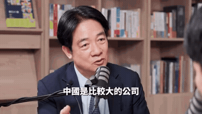 A Man In A Suit And Tie Is Talking Into A Microphone In Front Of A Bookshelf In A Library . GIF