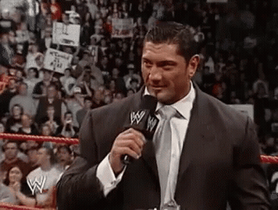A Man In A Suit And Tie Is Talking Into A Microphone In Front Of A Crowd . GIF