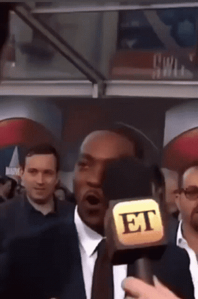 A Man In A Suit And Tie Is Talking Into A Microphone That Says Et GIF