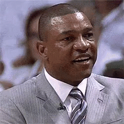 A Man In A Suit And Tie Is Talking Into A Microphone While Sitting In Front Of A Crowd . GIF