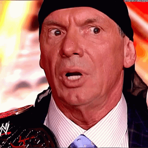 A Man In A Suit And Tie Is Talking Into A Microphone While Wearing A Black Headband GIF