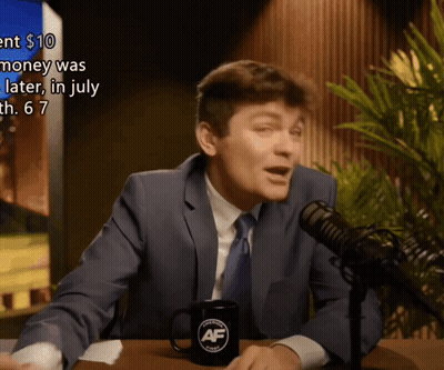 A Man In A Suit And Tie Is Talking Into A Microphone With A Mug That Says Af On It GIF