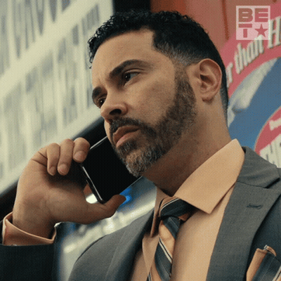 A Man In A Suit And Tie Is Talking On A Cell Phone In Front Of A Sign That Says Be Thankful GIF
